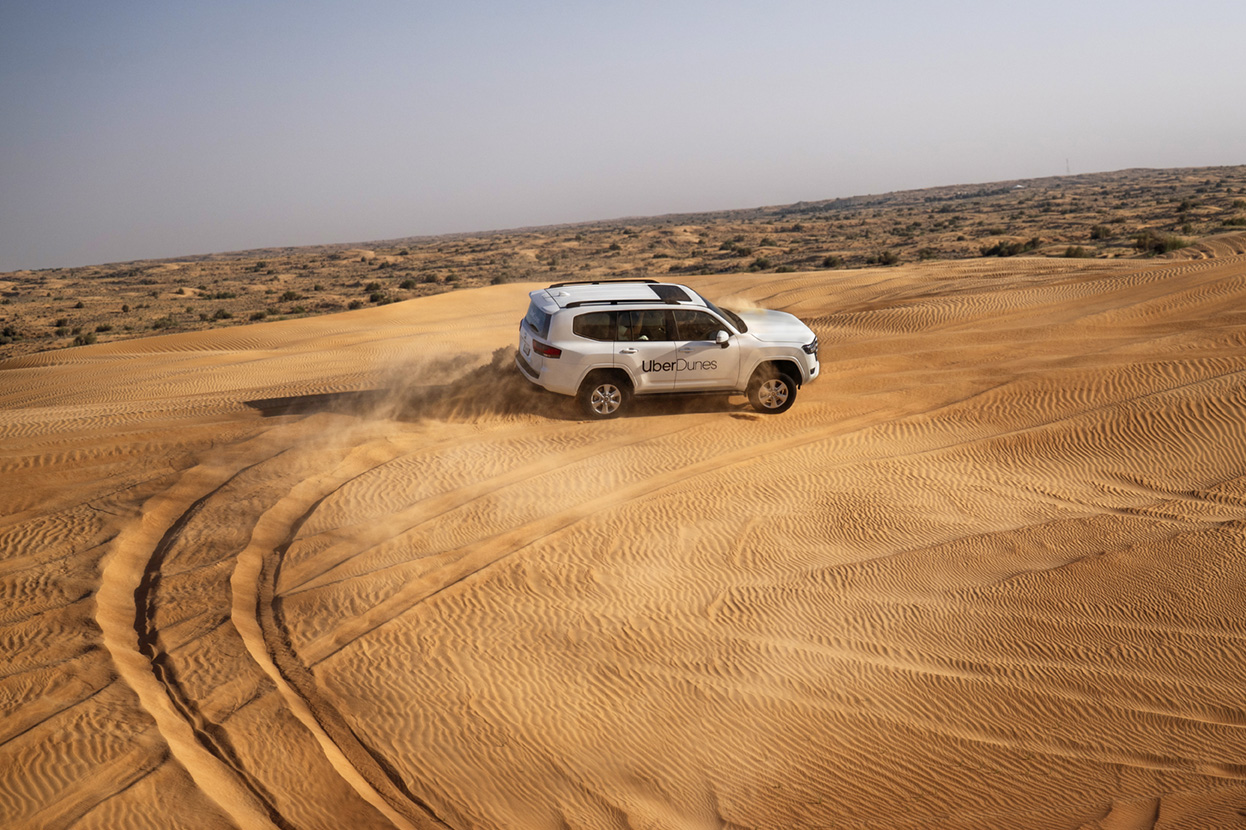Couple posing in front of UberDunes Land Cruiser on desert dunes, UAE